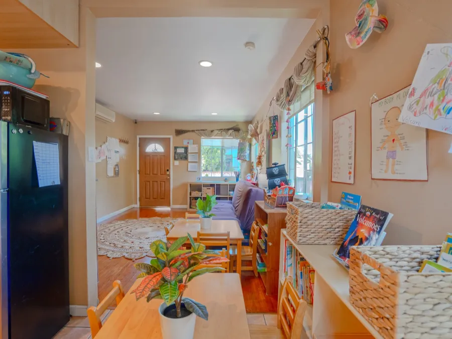 A bright, home-like preschool classroom with child-sized wooden furniture and learning materials on open shelves